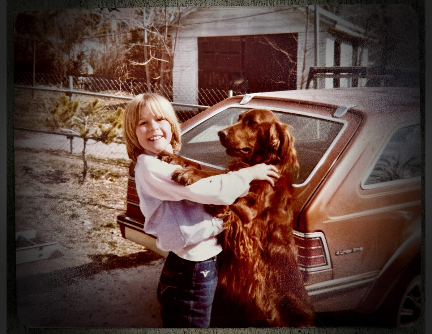 Smiling child hugging large brown dog by car